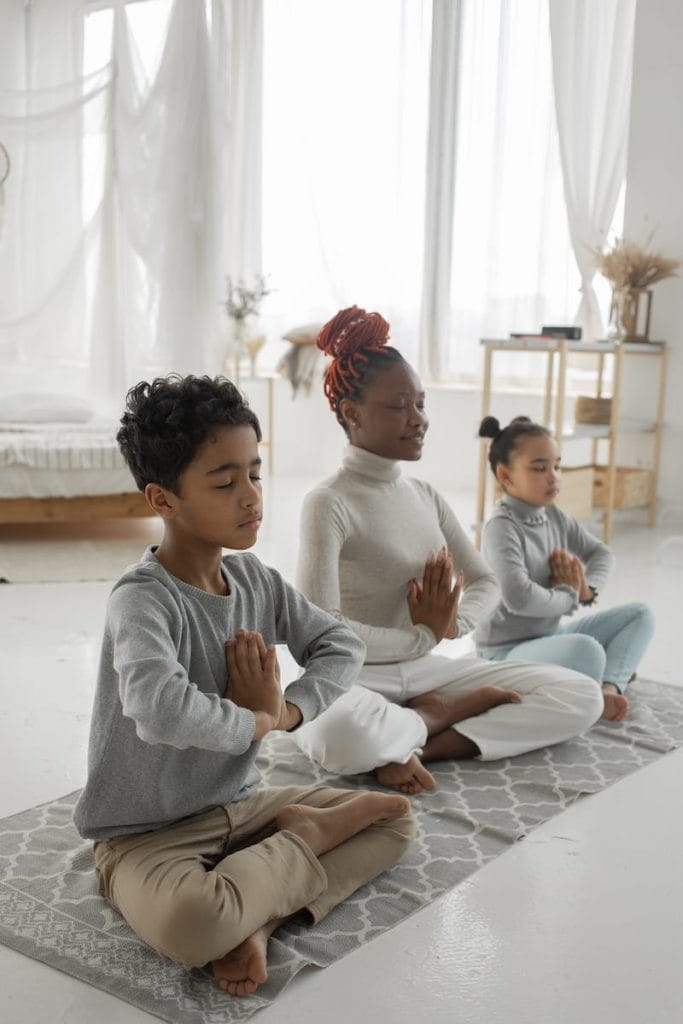 Cute ethnic children with young mom meditating together with closed eyes at home